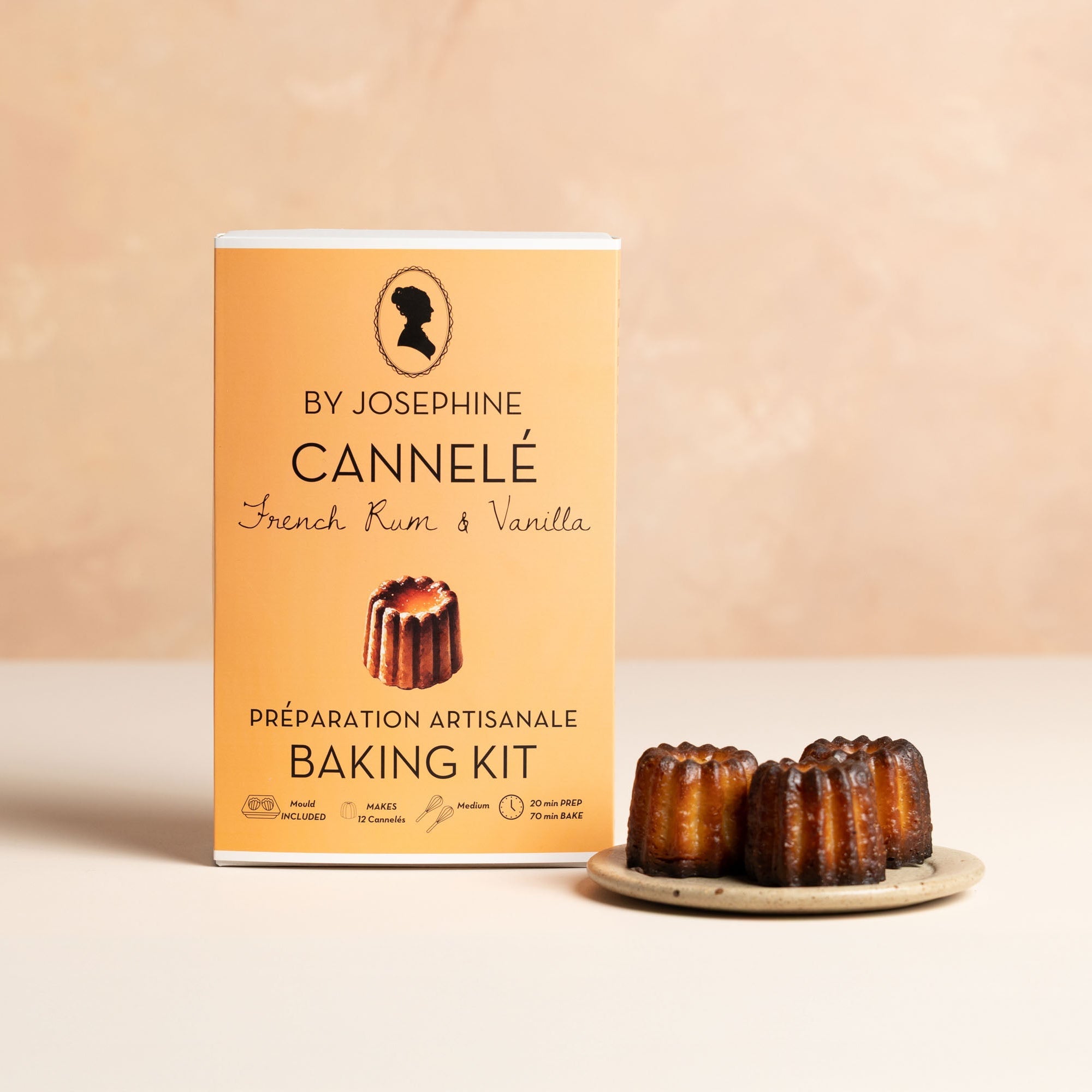 Canelé baking kit packaging with a plate of cannelés on a beige background