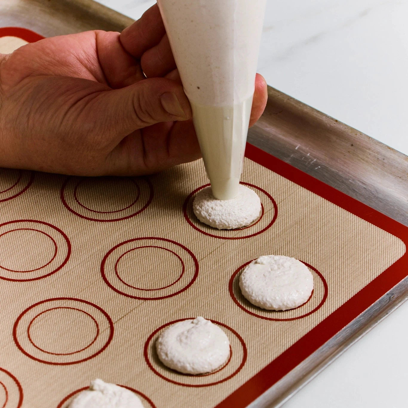Hand piping white batter onto a silicone mat with circular molds.